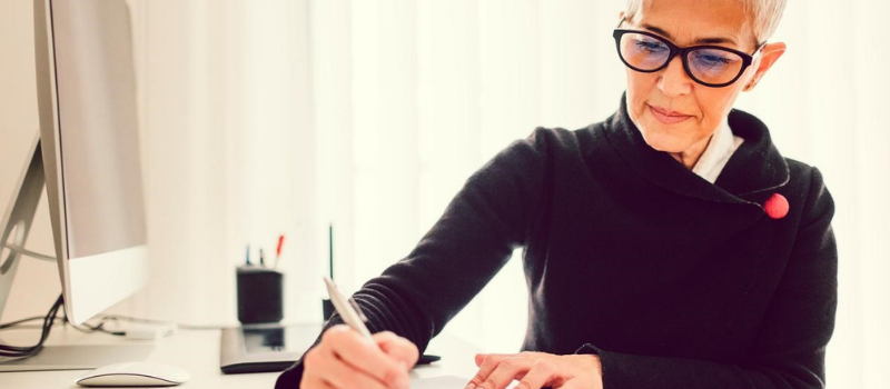 A female business professional sitting at a desk, writing. 