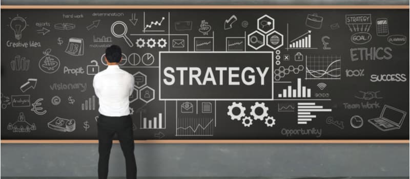 A man standing in front of a blackboard that says "strategy". 