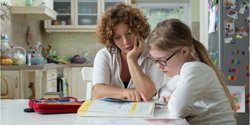 A mother helping her daughter with homework at the dining table.