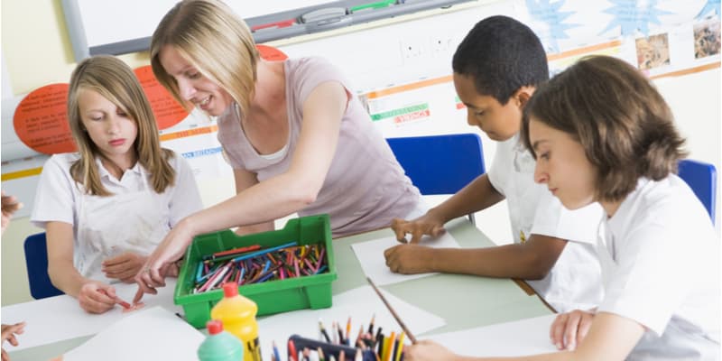 A female teacher working at the table with students doing artwork.