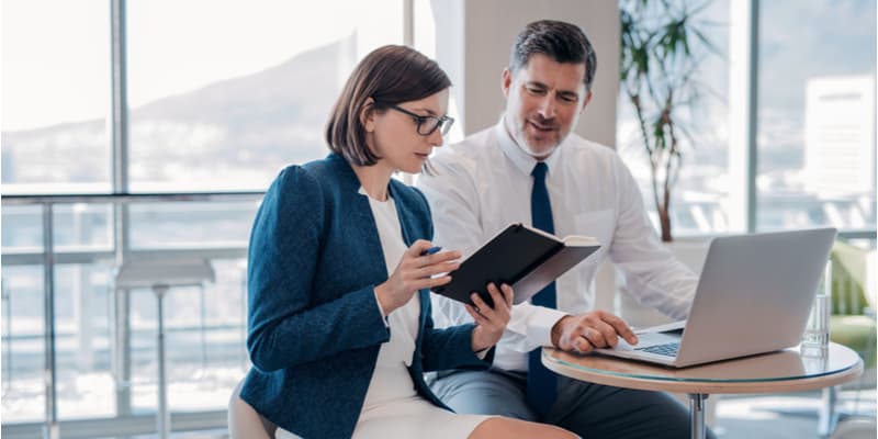 Two male and female business colleagues discussing a report on a tablet and taking notes. 