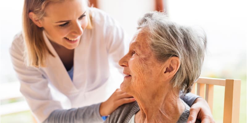 An aged care nurse and an older lady smiling at each other and chatting. 