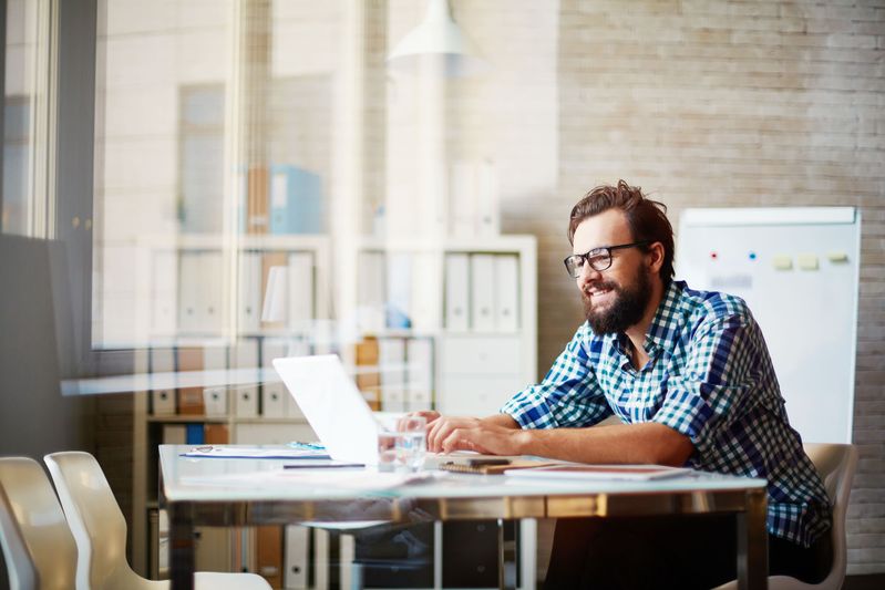 An SCU Online MBA student sits at a desk working on his laptop and smiling.