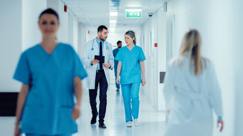 An SCU Master of Mental Health Nursing student walks down a hallway in a hospital, having a discussion with a doctor.