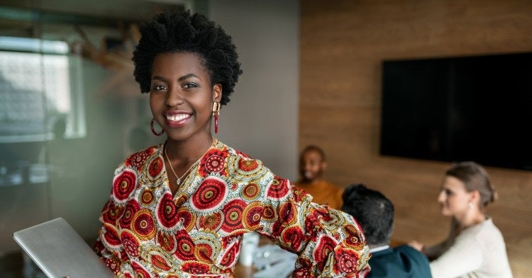 A finance manager holds a laptop and smiles.