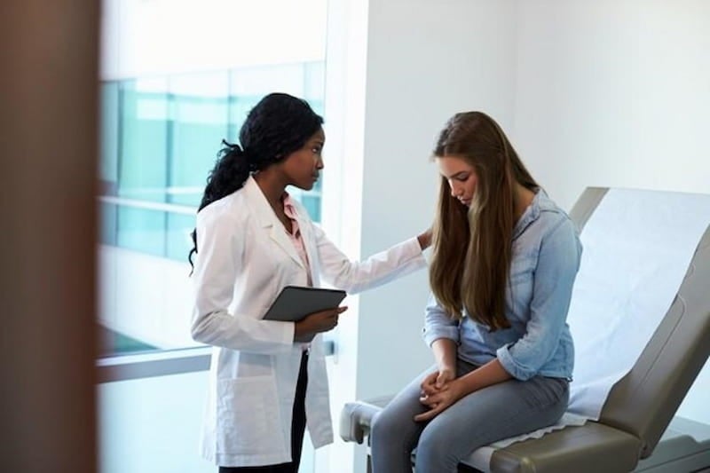 A mental health nurse comforts a patient seated in a medical facility exam room.