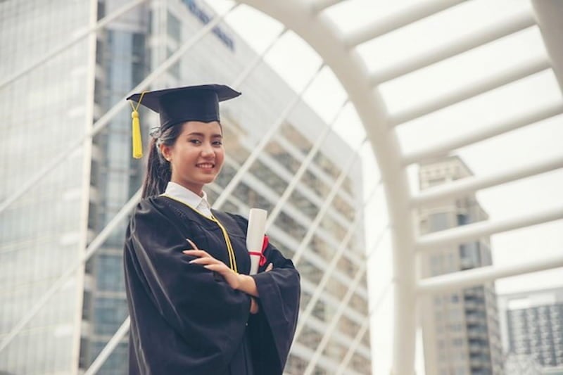 A smiling MBA graduate in a cap and gown holds a diploma.