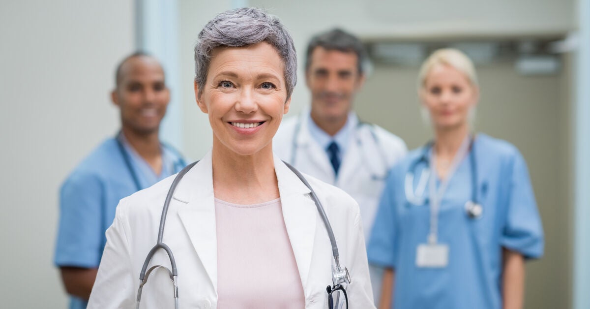 Portrait of smiling healthcare worker standing in hospital with team in background