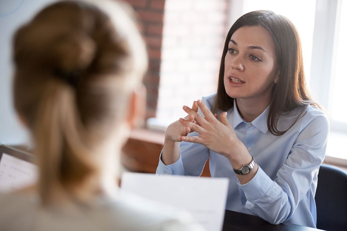 A female mental health student engages in conversation with another woman in a professional office setting, showcasing collaboration and communication