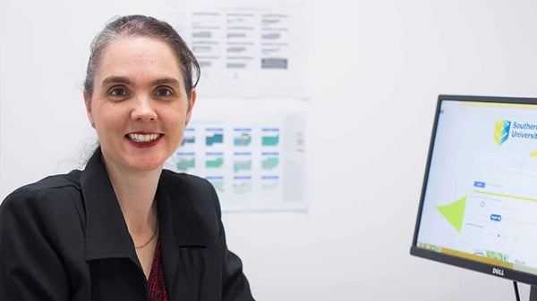 A woman seated at a desk, focused on her work in front of a computer, surrounded by office supplies and a notepad.