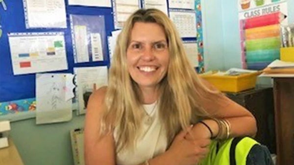 A woman seated in a classroom, wearing a backpack, engaged in learning or discussion with her surroundings.