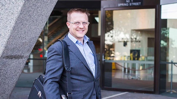 A man in a suit and tie stands confidently outside a modern building, showcasing professionalism and poise.