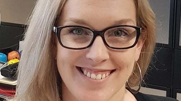 A woman wearing glasses and a black shirt smiles warmly, exuding confidence and approachability.