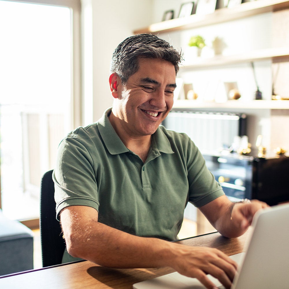 A man smiles contentedly while working on his laptop computer, showcasing a moment of joy and productivity.