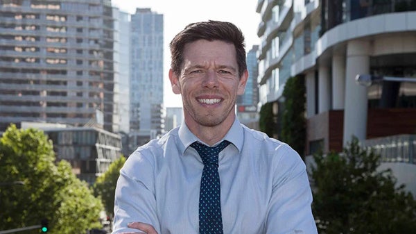A man in a shirt and tie stands confidently in front of a bustling city skyline, showcasing urban professionalism.