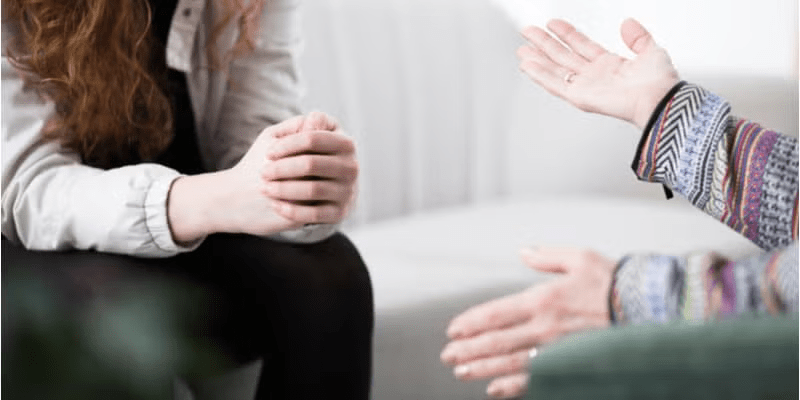 A closeup of an anxious teenager clasping their hands while talking with a therapist.