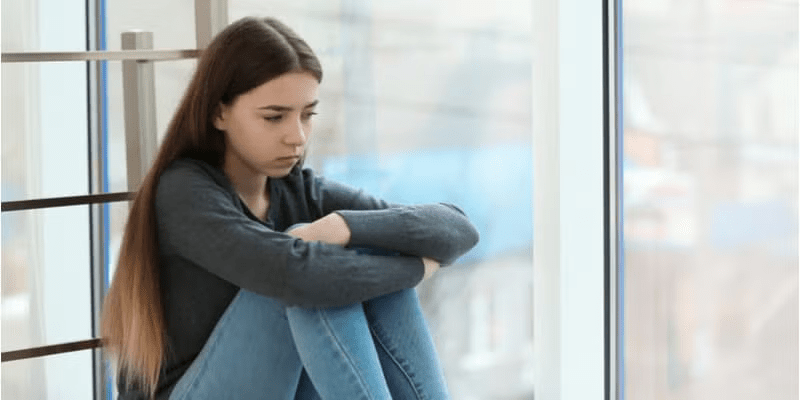 An upset teenage girl sat on the floor holding her knees to her chest. 