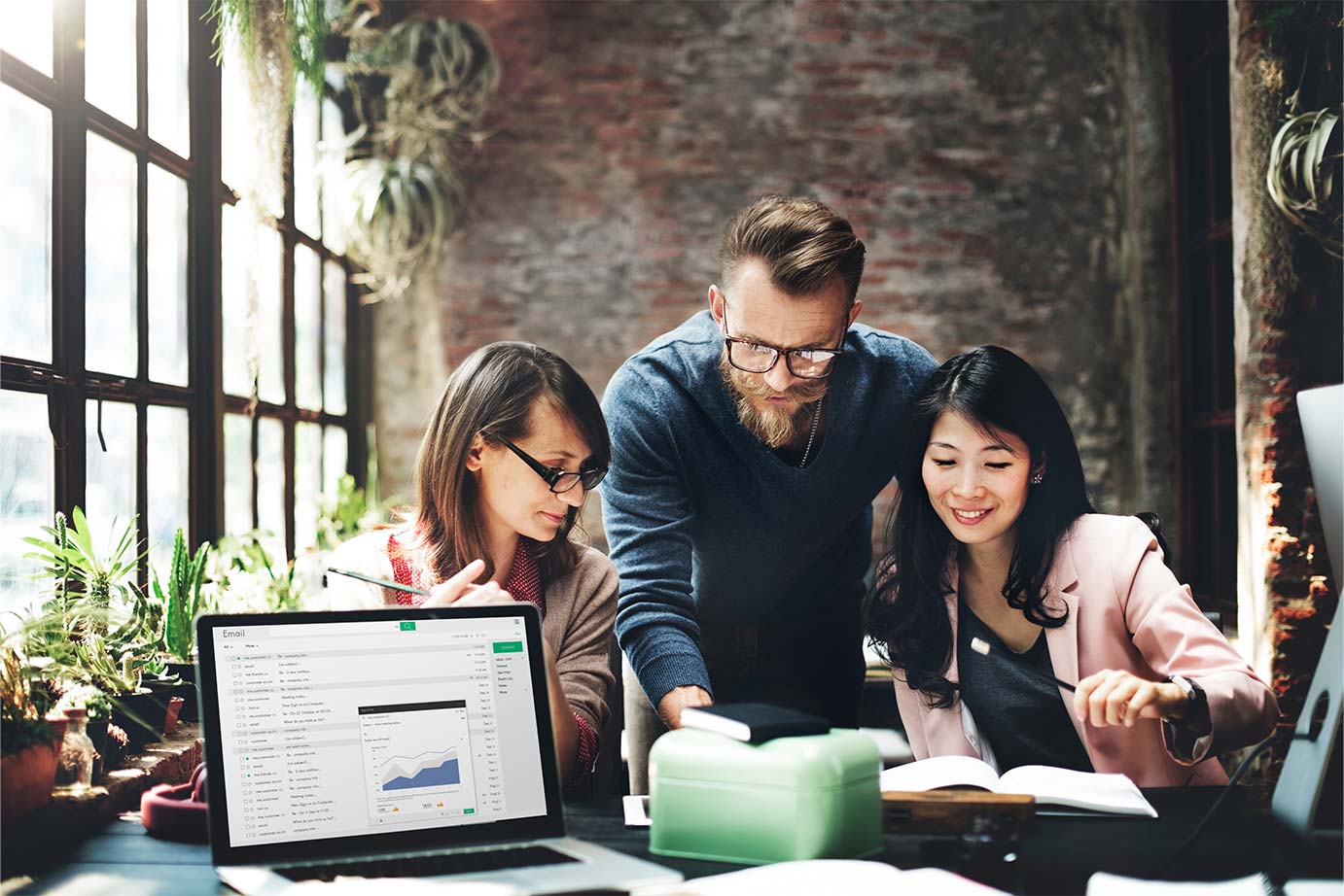 Three individuals collaborating on a laptop in a modern office setting, focused on their work and sharing ideas.