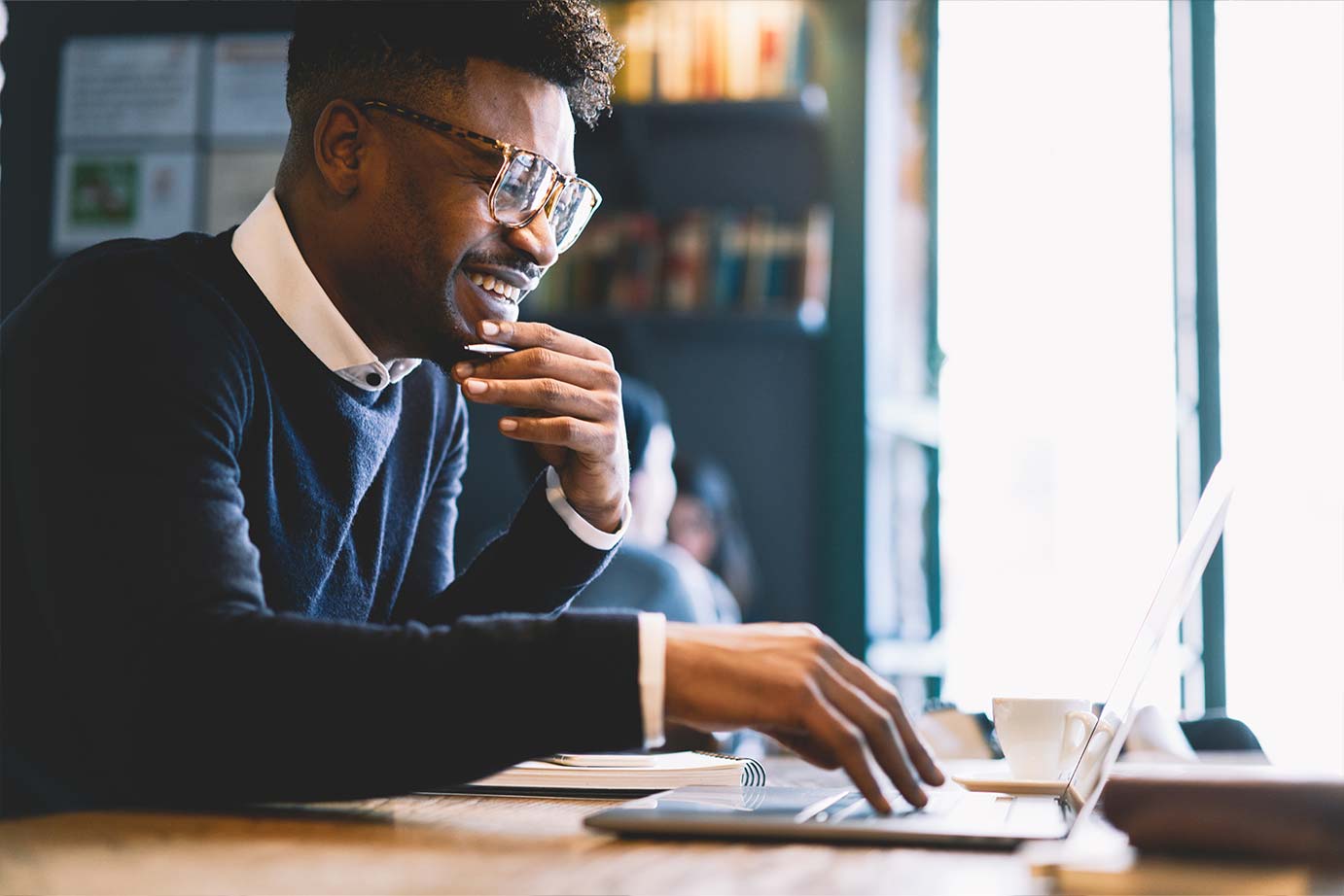 A man wearing glasses is focused on his laptop, engaged in work at a desk.