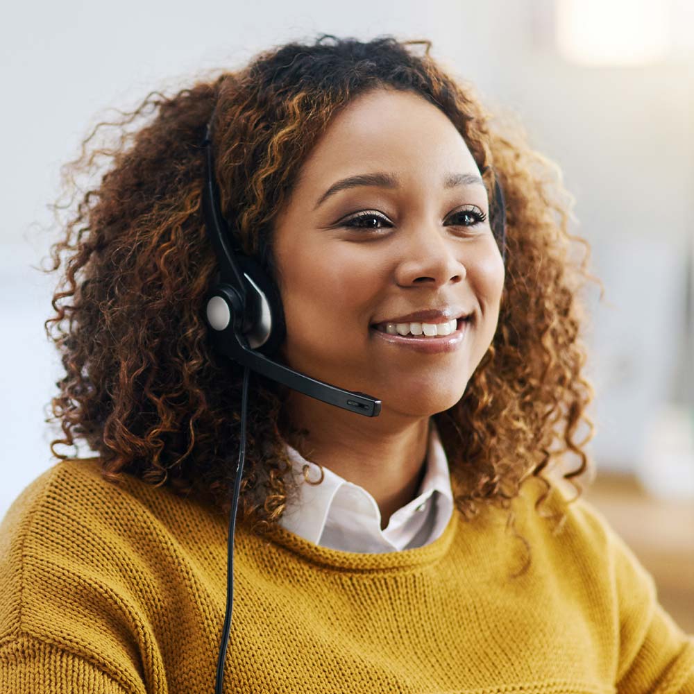 A woman with a headset, smiling warmly, exuding a friendly and approachable demeanour.