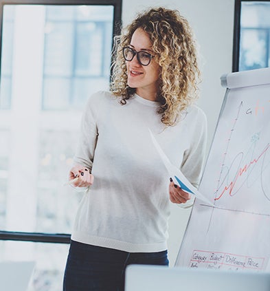 A woman stands confidently in front of a whiteboard, ready to present her ideas and engage with her audience.