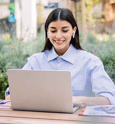 A woman seated at a table, focused on her laptop, engaged in work or study in a cozy environment.