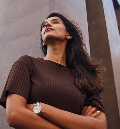 A woman stands confidently with her arms crossed in front of a modern building, showcasing a poised demeanour.