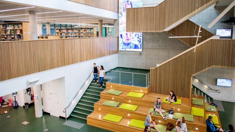 A bustling library filled with people, some seated on the grand staircase, immersed in reading and study.