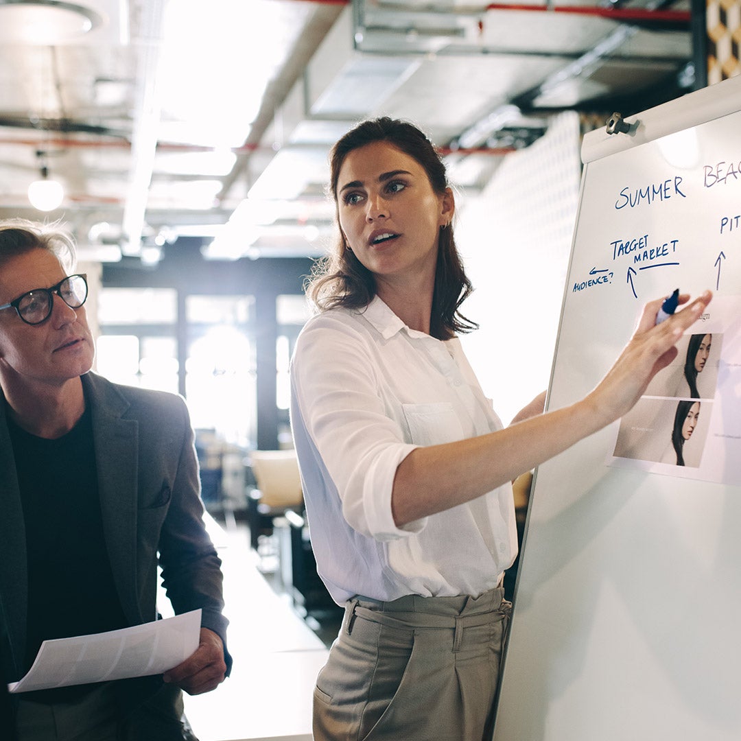 A man and woman stand together in front of a whiteboard, engaged in discussion or presentation.