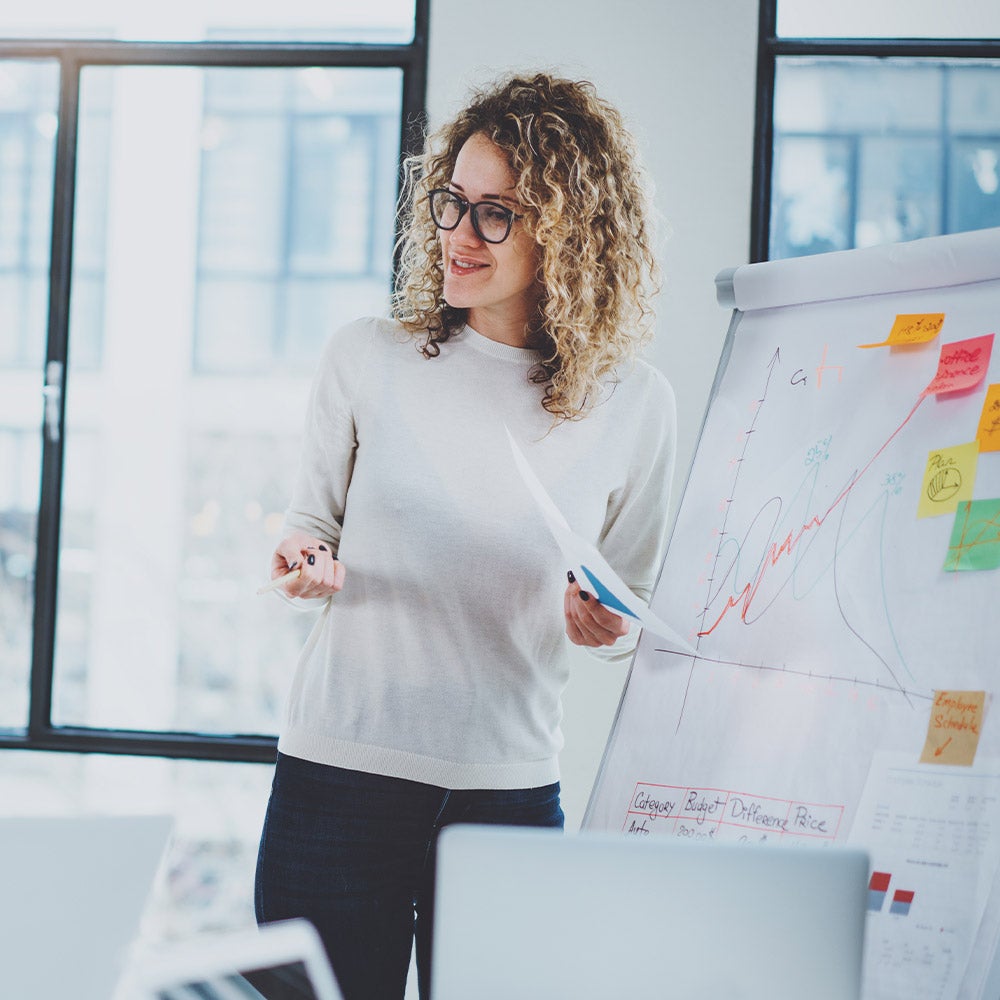 A female project management student stands confidently in front of a whiteboard, ready to present her ideas and engage with her audience