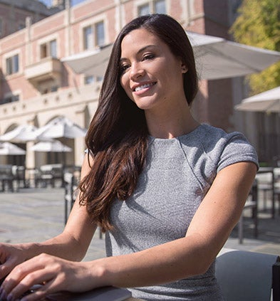 A woman smiles brightly while standing in front of a modern building, showcasing a sense of joy and confidence.