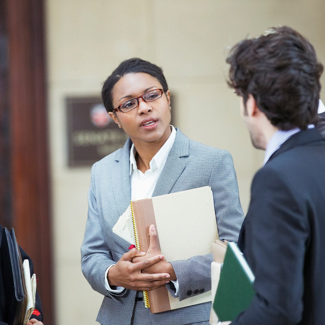 A woman in a business suit engages in conversation with two colleagues in a professional setting.