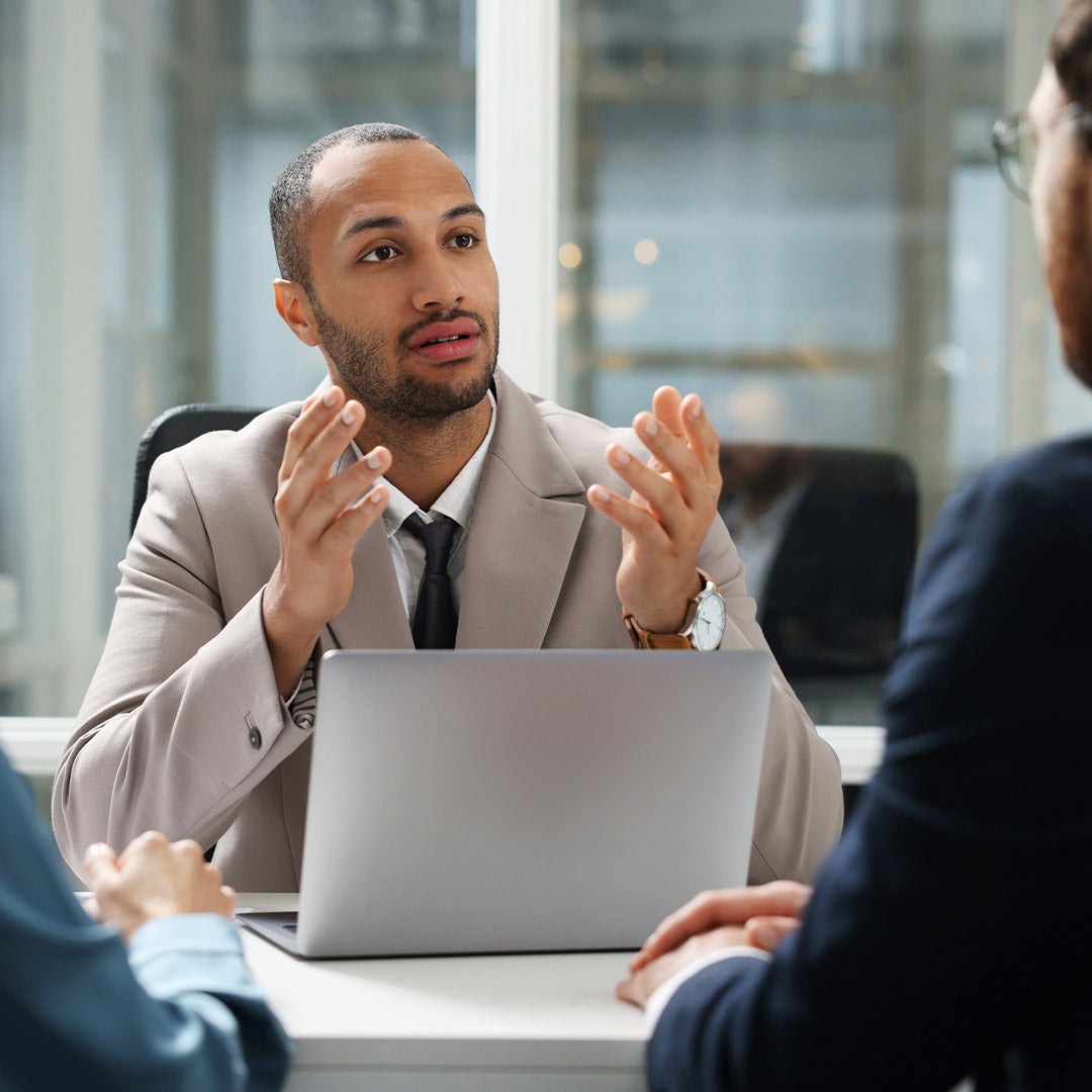 A man in a suit engages in conversation with two individuals in a professional setting.