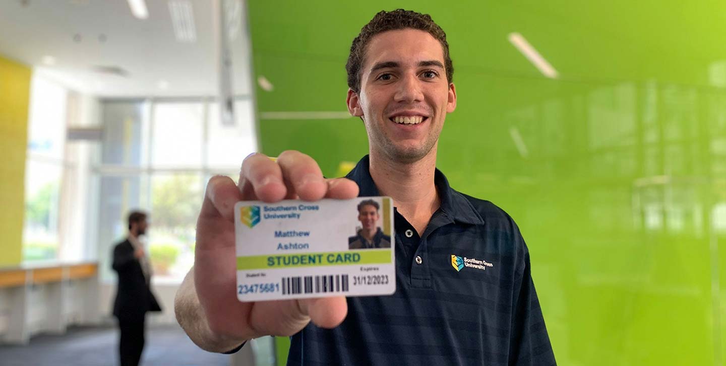 A man displays a green ID card against a matching green wall, emphasising the card's colour and his confident stance.