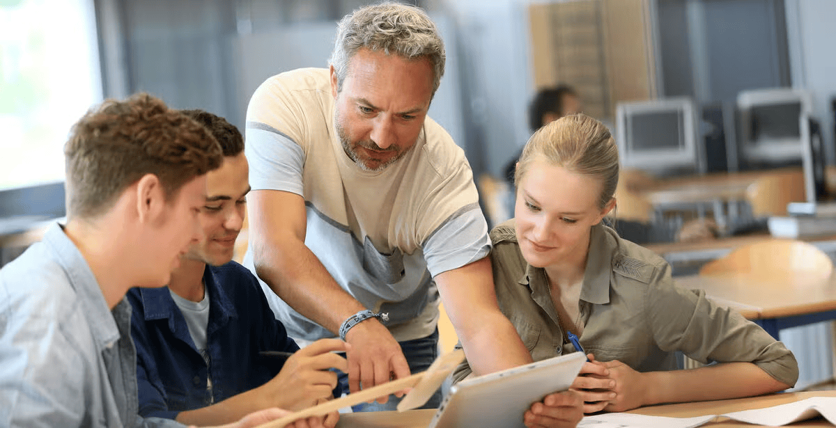 Male teacher helping group of students at school