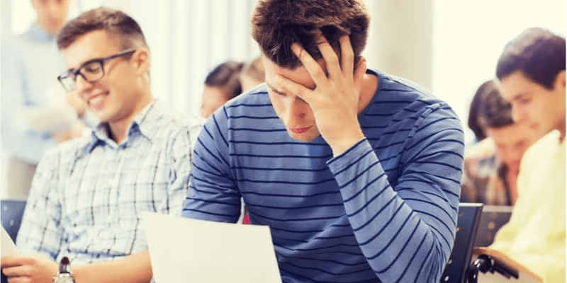 student stressed with paper and pen sitting with group of classmates