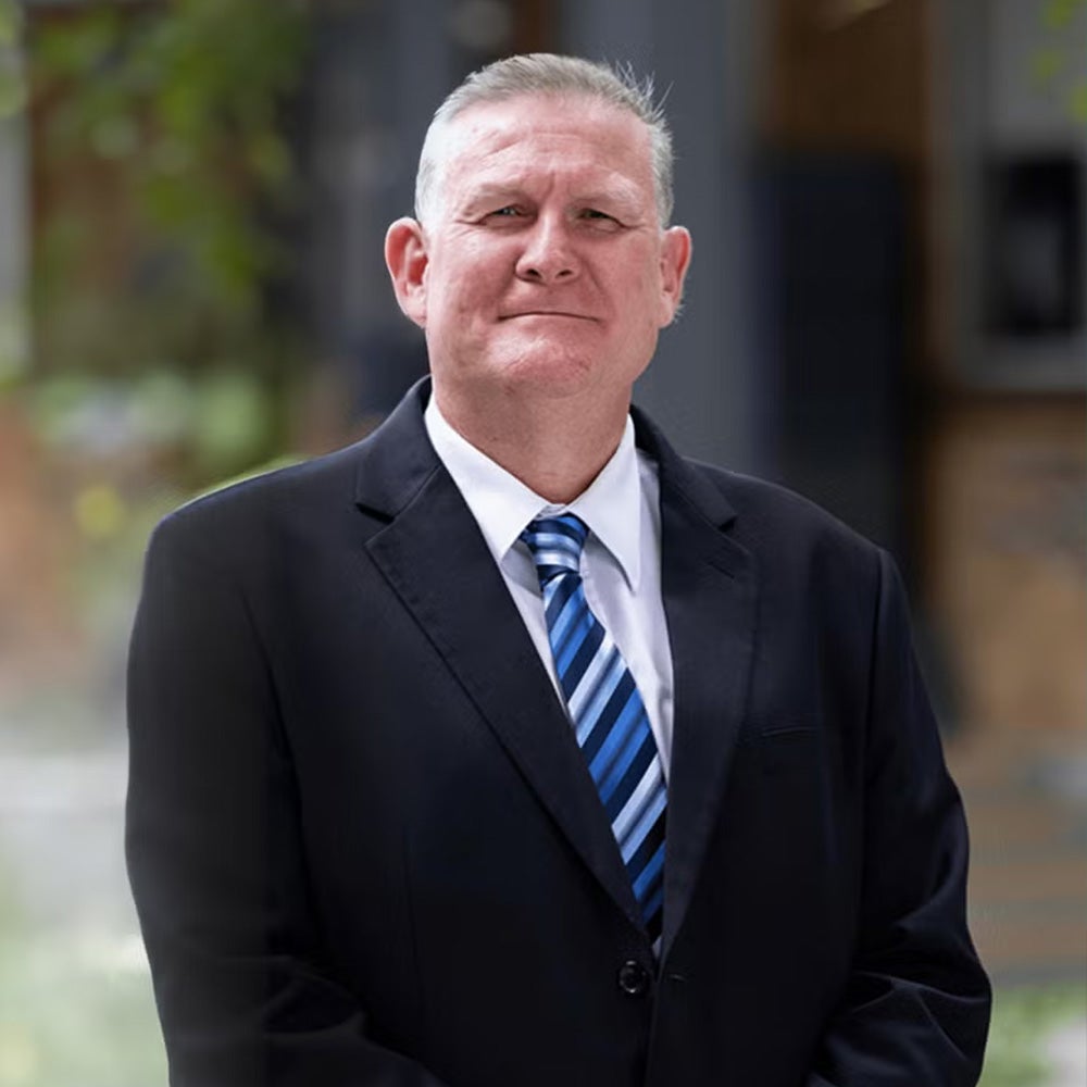 A man in a suit and tie stands confidently in front of a modern building, exuding professionalism and poise.