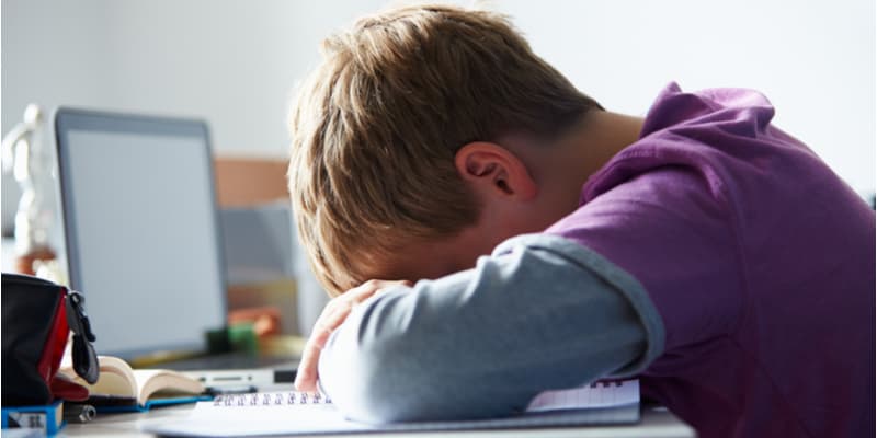 A boy sat at desk with his head on his hands because he feels sad.