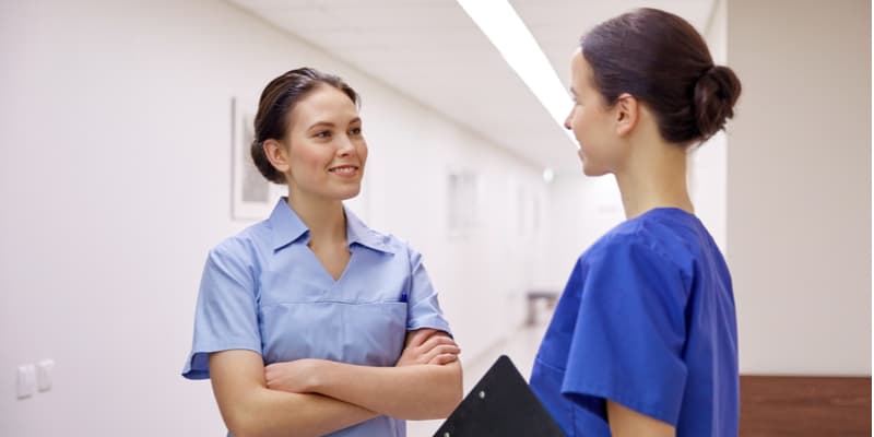 Two female nurses exchanging ideas in corridor.