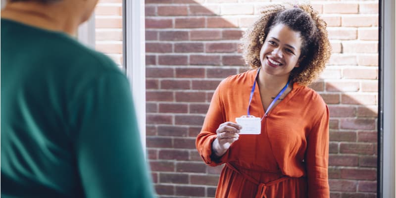 A female social services worker smiling at the front door, showing her name badge. 