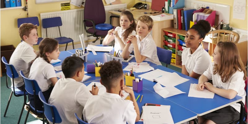 A group of young students sat around a table talking with each other while doing an activity.