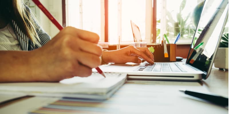 A legal writer making some notes on paper next to their laptop.