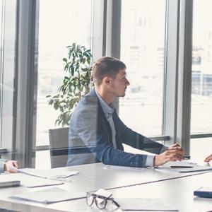 A group of business professionals engaged in discussion at a table, with a large window providing natural light behind them.