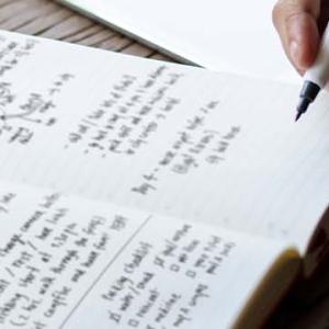 A woman focused on writing in a notebook, capturing her thoughts with a pen in a serene environment.