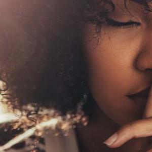 A woman with her hand on her mouth and a finger to her lips, signalling for silence or contemplation.