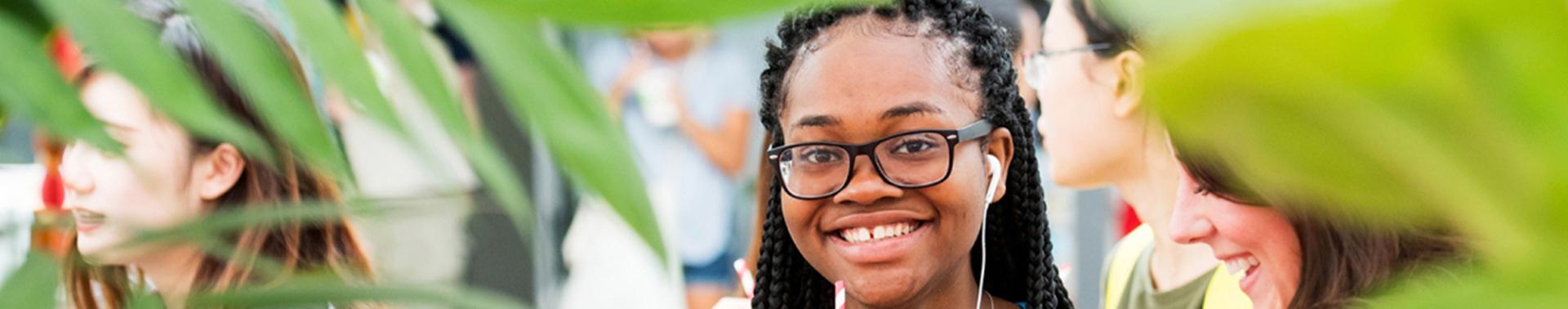 A woman smiles joyfully while holding a drink, surrounded by a lively group of people in the background.
