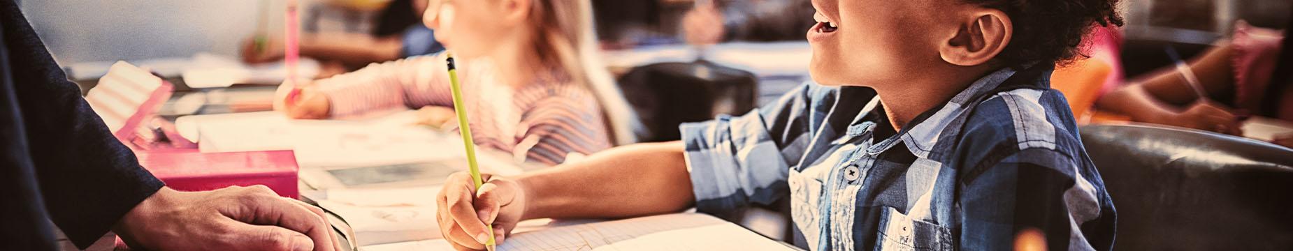 A soft-focus image showing a child sitting at a desk, absorbed in an activity, with unclear details in the background.