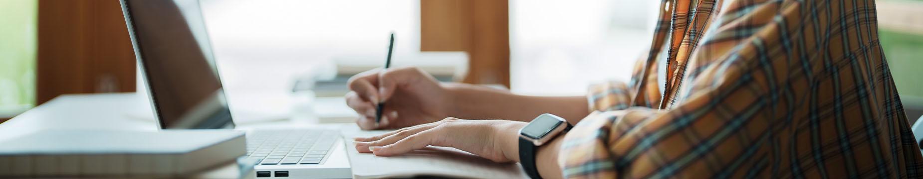 A person focused on typing on a laptop computer, with hands positioned on the keyboard and screen illuminated.
