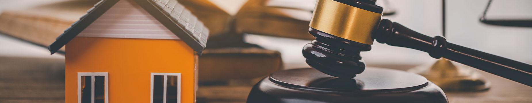 A gavel rests beside a house model on a table, symbolising the intersection of law and real estate.