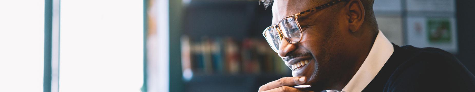 A man wearing glasses is intently focused on his laptop screen, engaged in his work or research.
